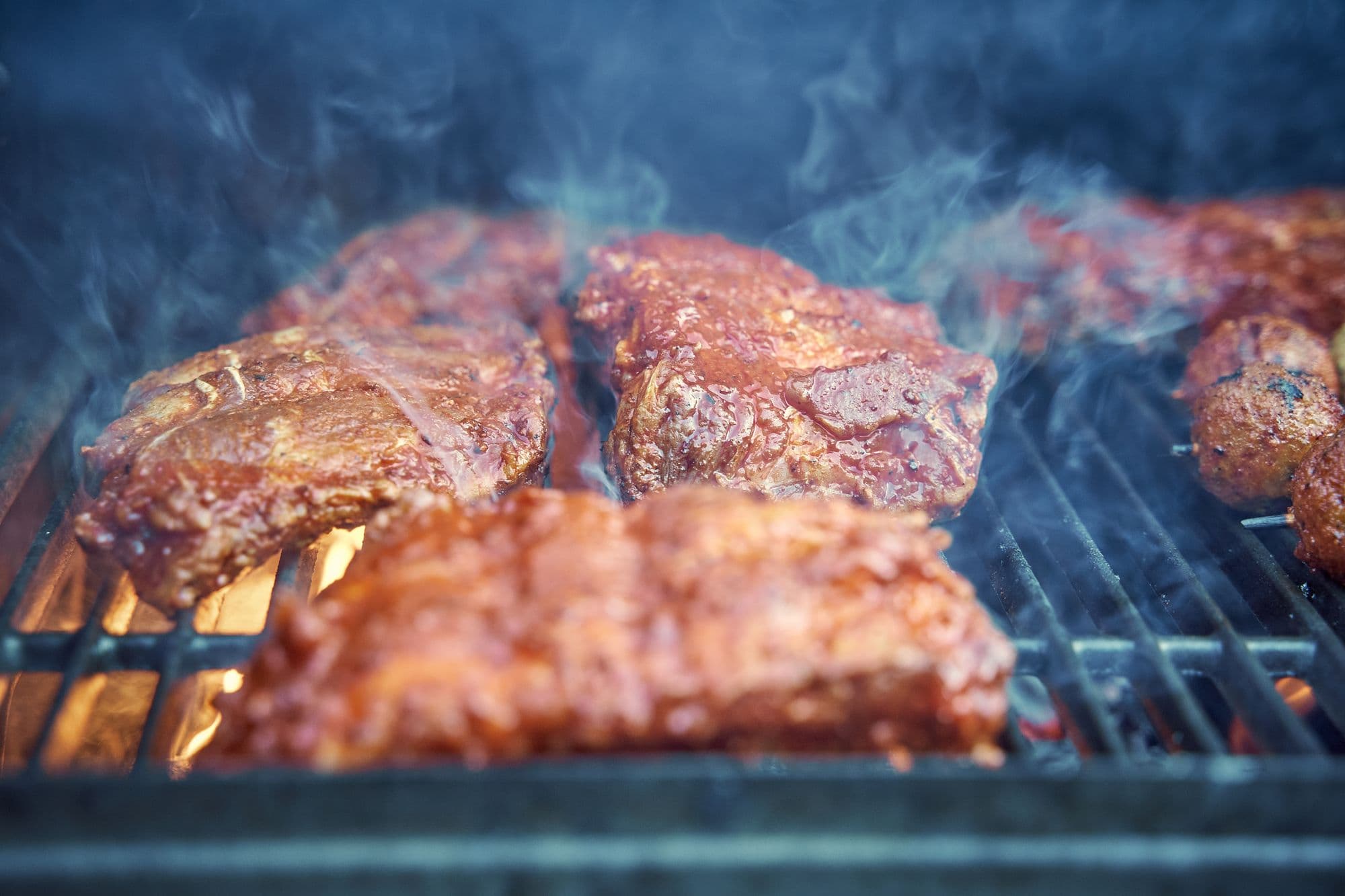 Sauced pork ribs on a grill grate with blue smoke rising