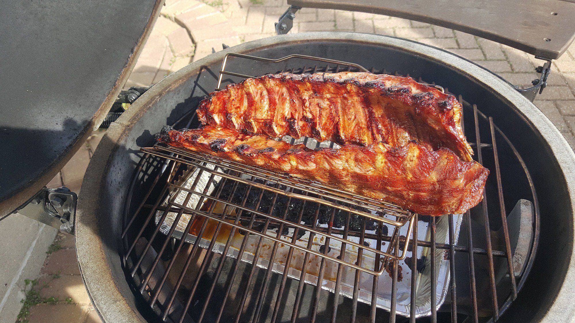 Rack of glazed ribs on a raised grate inside an open green kamado grill on a brick patio