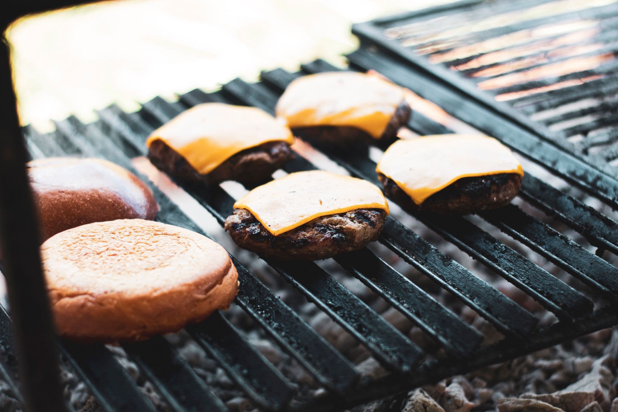 Cheeseburger patties with melted cheese and toasted buns on a cast-iron grill grate