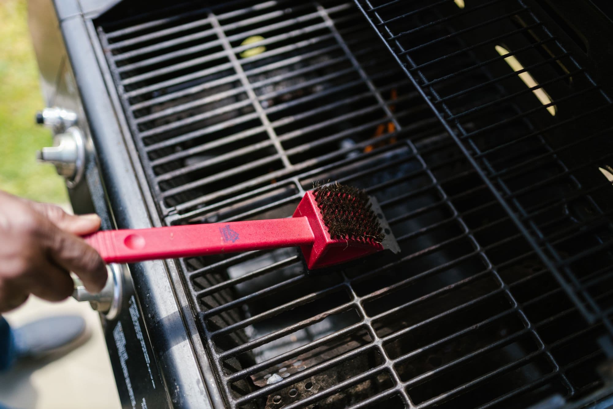 Hand scrubbing gas grill grates with a red wire grill brush