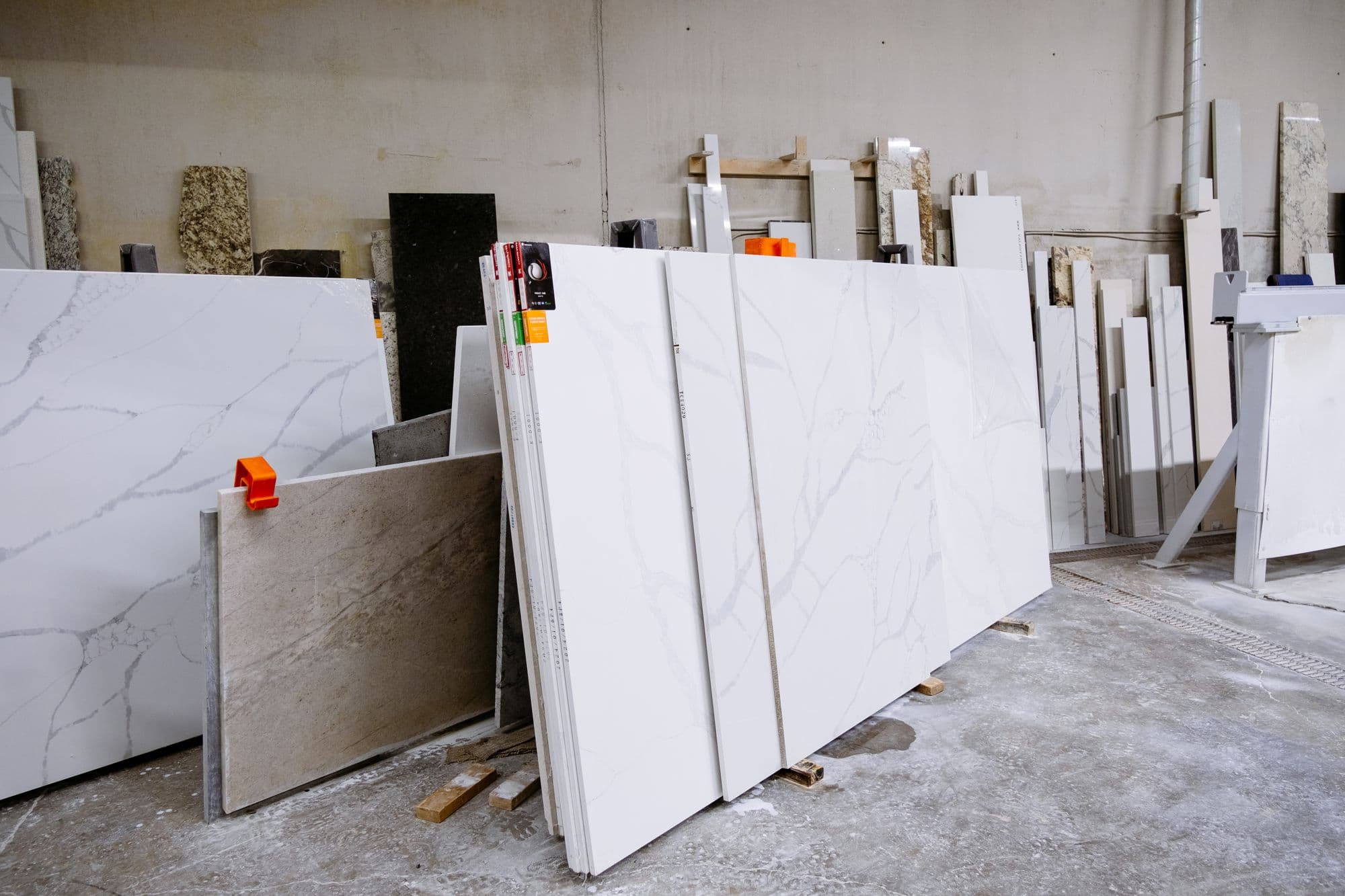 Large white veined countertop slabs and granite remnants standing on racks in a fabricator's yard