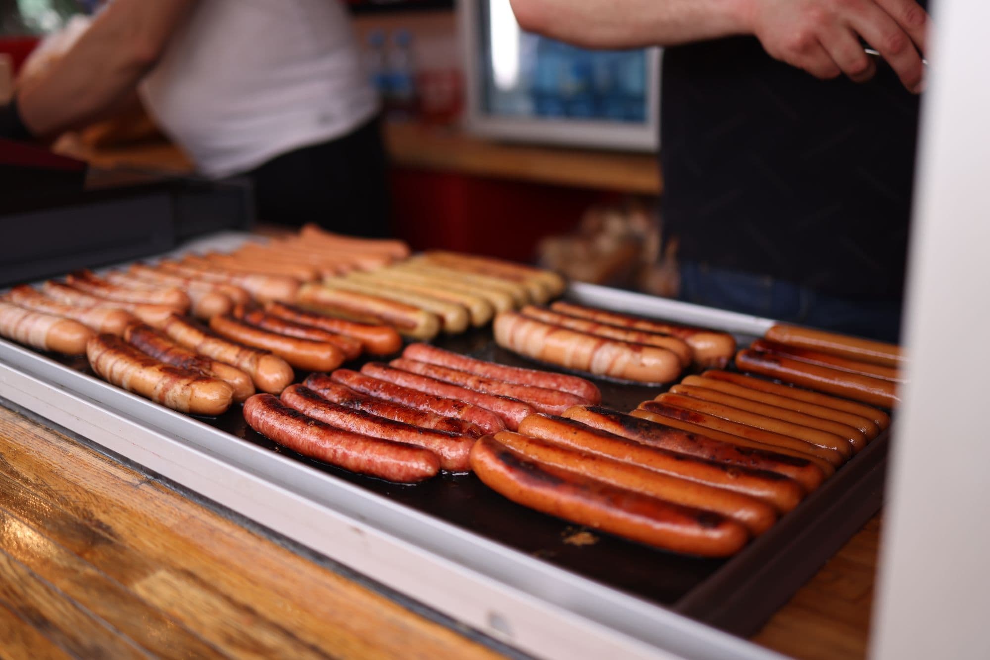 Rows of browned sausages cooking on a flat-top griddle at an outdoor stand