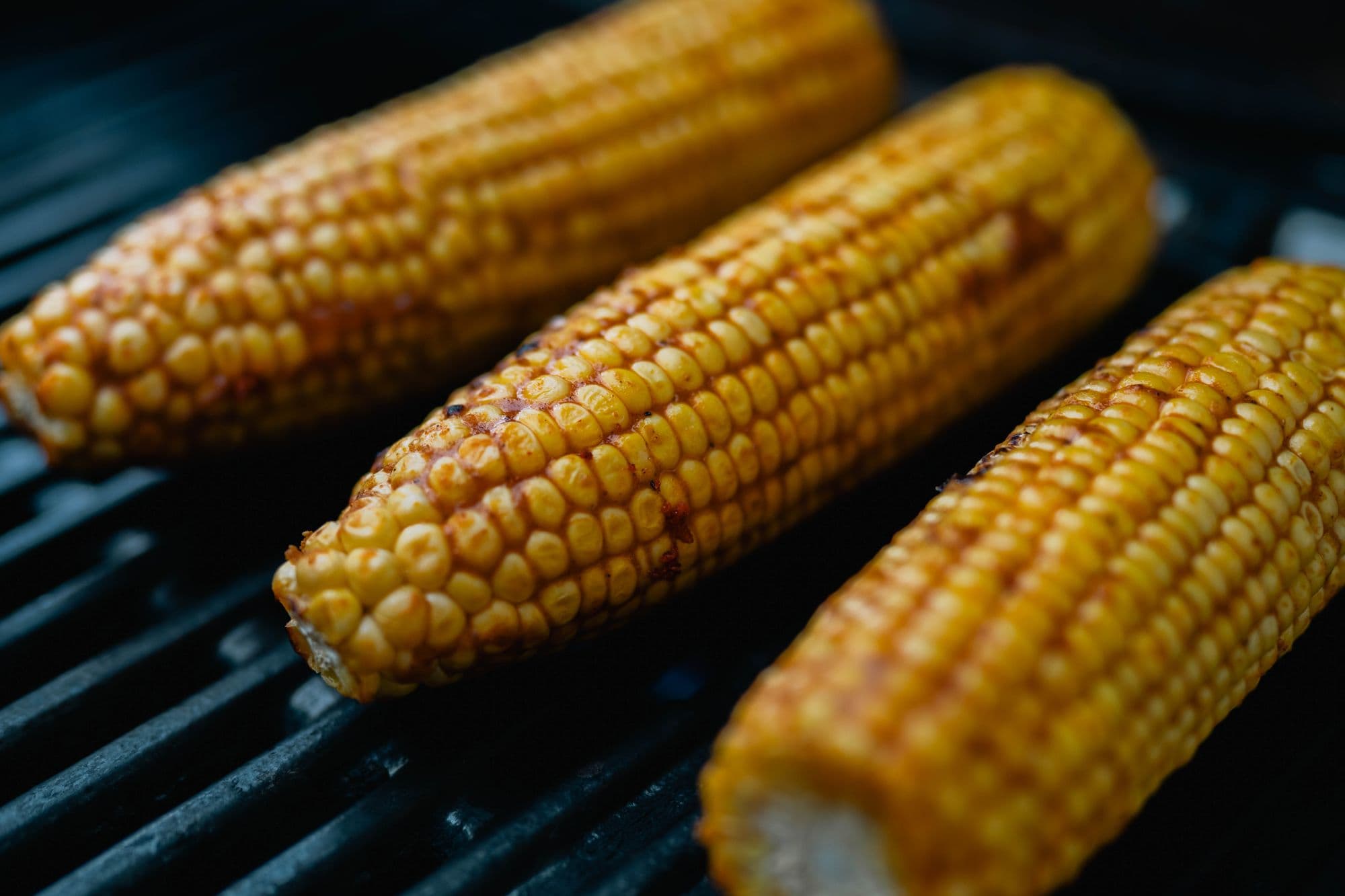 Three charred ears of corn on the cob on a black grill grate