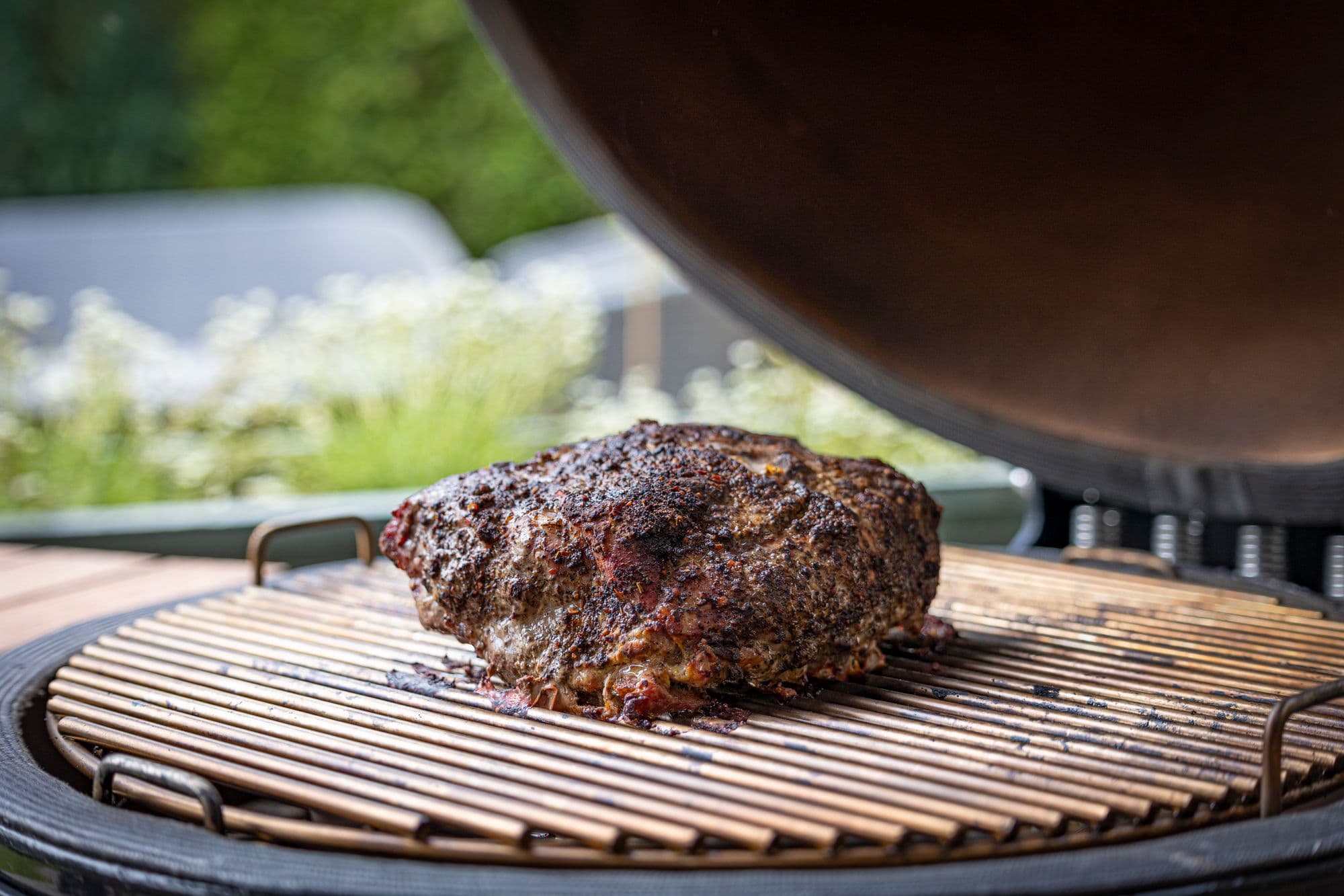 Seasoned beef roast on the round grate of a kamado-style grill with the domed lid raised