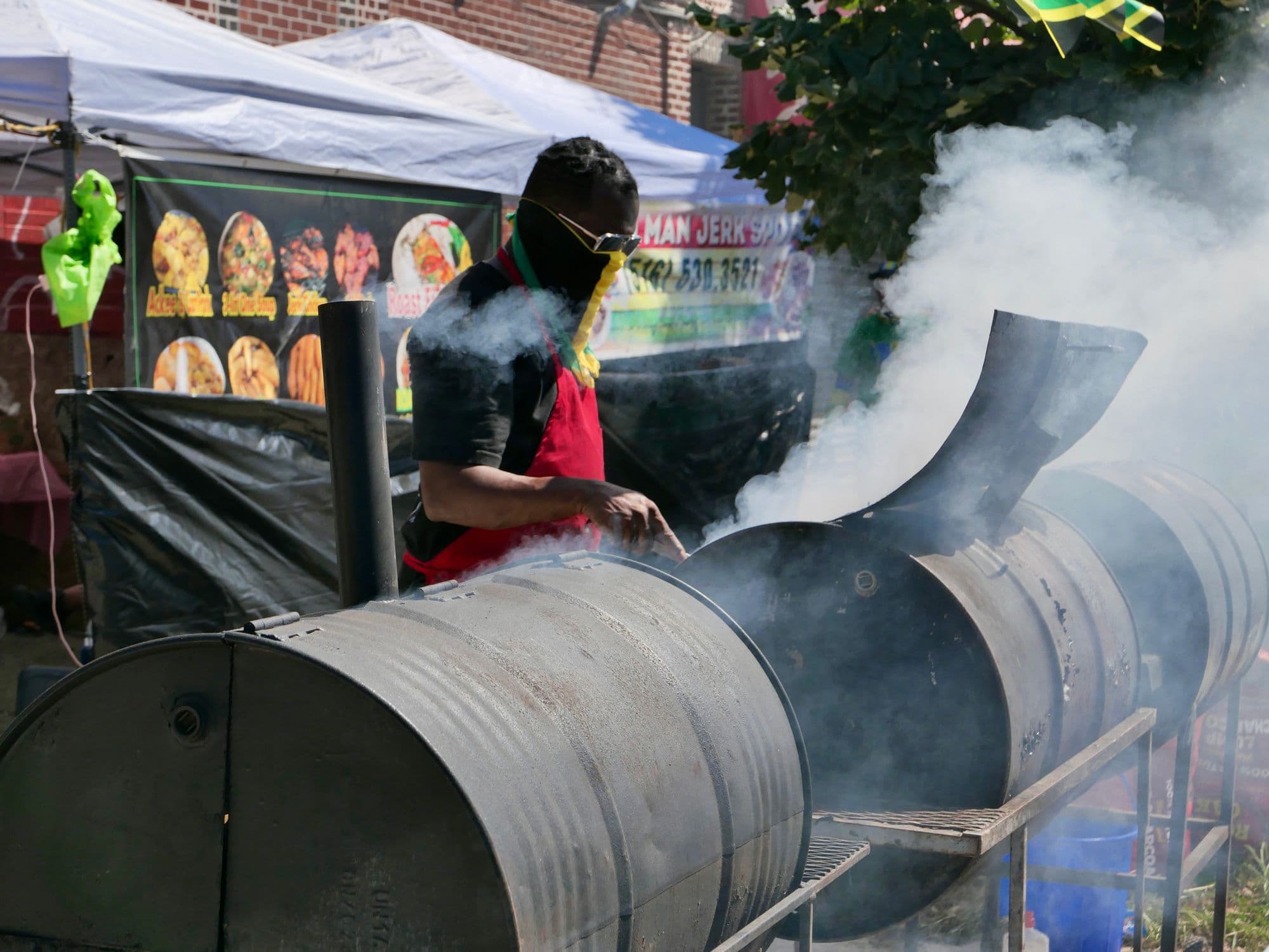 Large barrel-style offset smoker pouring white smoke at an outdoor food festival, with a cook tending it