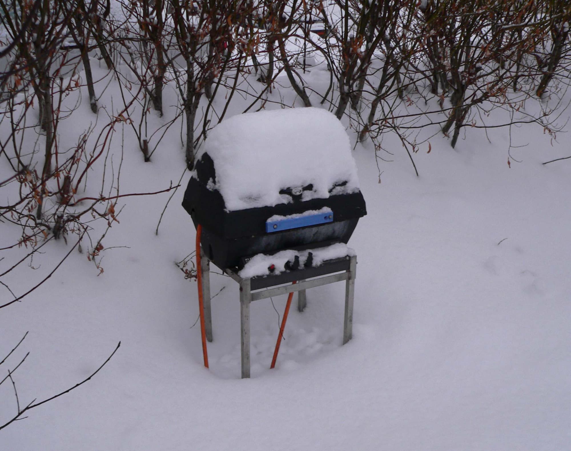 Small propane gas grill on a stand covered in a thick layer of snow