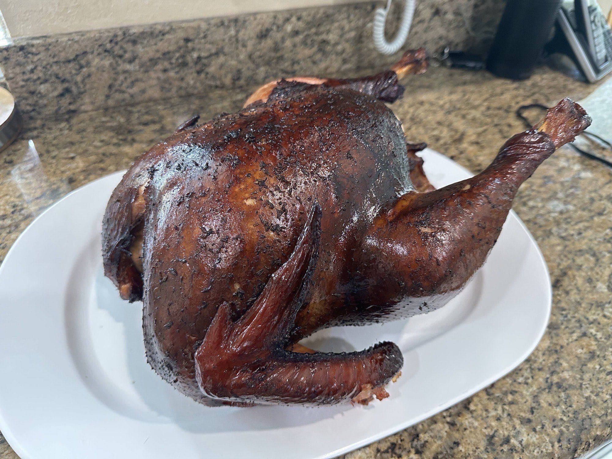 Whole smoked turkey with dark mahogany skin on a white platter on a granite countertop