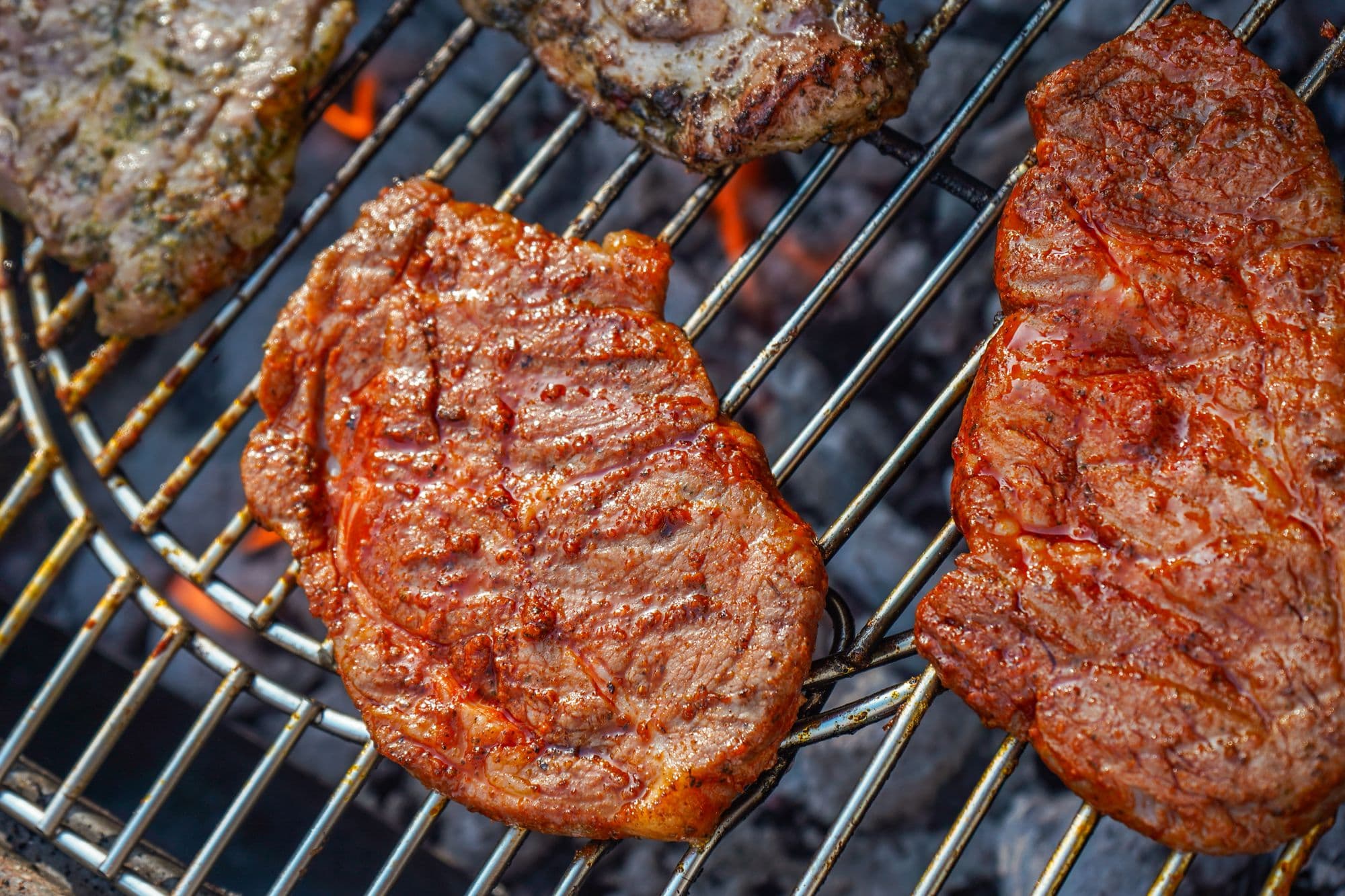 Two marinated steaks on a round wire grate over glowing charcoal