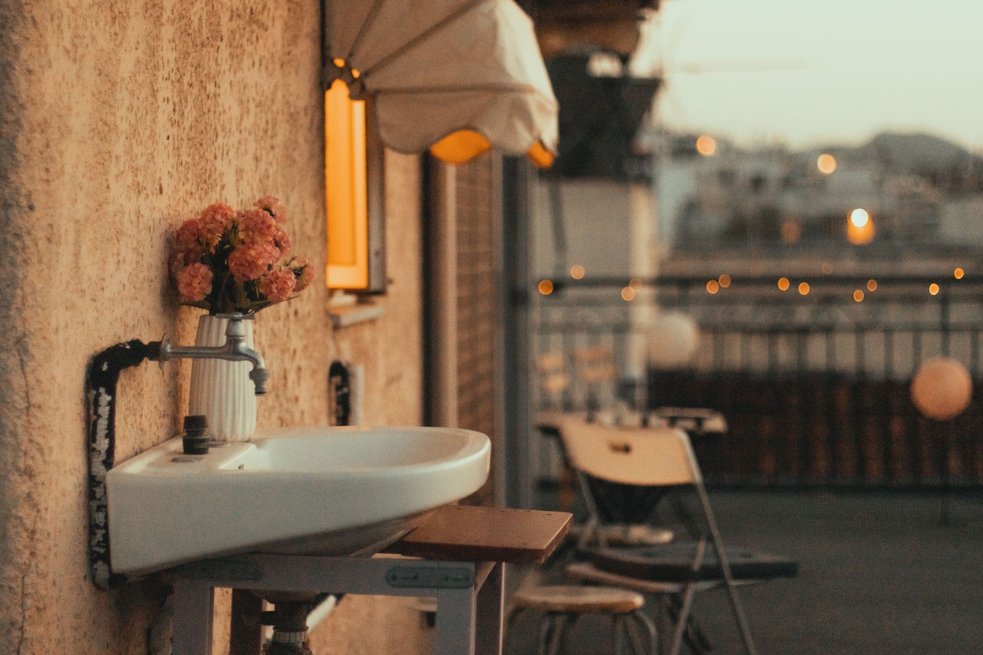 Wall-mounted ceramic sink with a vase of flowers on an evening terrace with string lights