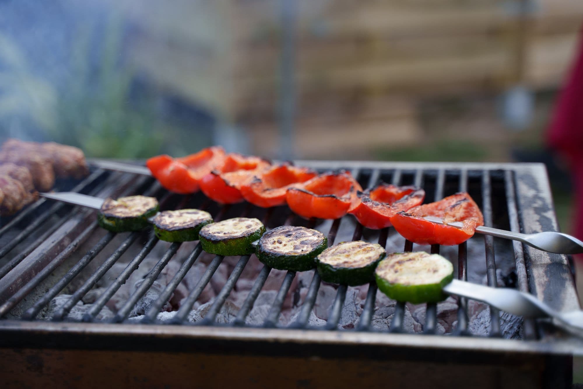Zucchini and red pepper skewers on a charcoal grill grate